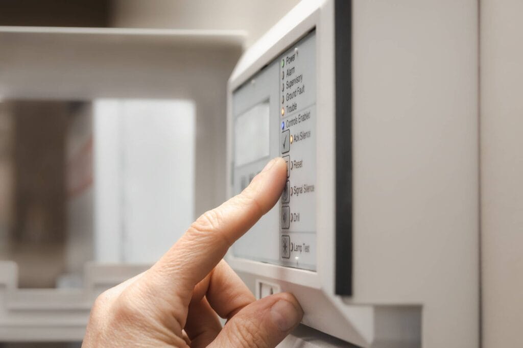 A close-up of a hand pressing a button on a control panel of a household appliance, possibly a washing machine or dishwasher. The panel has several labeled buttons and a digital display.